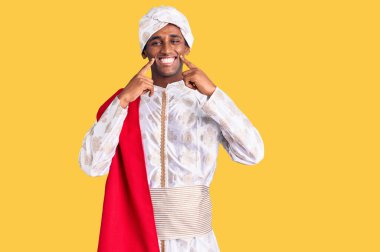 Gelenek giyinmiş Afrikalı yakışıklı bir adam Sherwani sari elbiseleri giyiyor ağzı açık gülümsüyor, parmakları işaret ediyor ve neşeli bir gülümseme sergiliyor. 