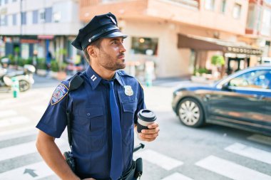 Genç İspanyol polisi ciddi bir ifadeyle polis üniforması giyiyor. Kasaba caddesinde dikilmiş kahve içerken.
