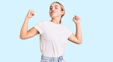 Genç, güzel, sarışın, sıradan beyaz tişörtler giyen, gururla gülümseyen kol kaslarını gösteren bir kadın. fitness konsepti. 