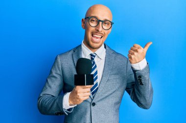 Sakallı kel bir adam mikrofon tutuyor. Parmağını yana kaldırıyor. Ağzını açıp gülümsüyor. 