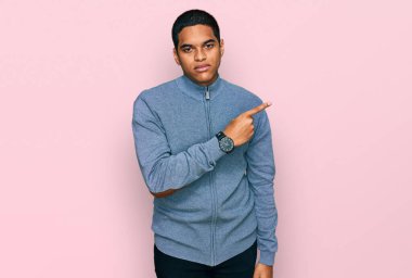 Gündelik kazak giyen genç, yakışıklı İspanyol bir adam, elini kaldırıyor ve reklamını yapıyor, ciddi ve sakin bir yüz ifadesi var. 