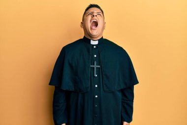 Sarı arka planda dikilen genç Latin papaz öfkeli ve öfkeli bağırıyor öfkeyle bağırıyor. öfke ve agresif konsept. 
