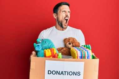 Genç ve yakışıklı bir adam oyuncaklarla dolu bir bağış kutusu tutuyor kızgın ve öfkeli çığlıklar atıyor, öfkeyle bağırıyor. öfke ve agresif konsept. 