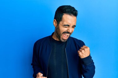 Gündelik giysiler giyen genç İspanyol adam şaşkınlık ve şaşkınlık içinde kollarını kaldırarak ve gözlerini kapayarak başarıyı kutluyor. 