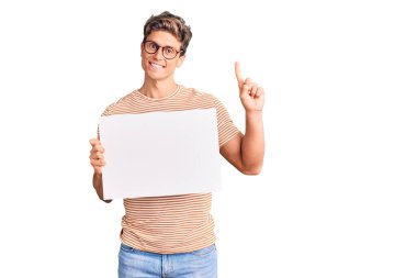 Elinde boş afiş tutan genç yakışıklı bir adam bir fikre ya da soru işaretine şaşırdı ve mutlu bir yüzle işaret etti. 