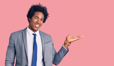 Afro saçlı, iş ceketi giyen, neşeli gülümseyen ve avuç içi kameraya bakan yakışıklı Afro-Amerikan adam.. 