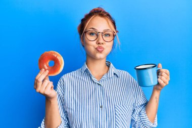 Genç kızıl saçlı kadın kahvaltısını çikolatalı çörek ve komik suratlı kahve şişiren yanaklarla yapıyor. Ağzı havayla şişer, havayı yakalar.. 