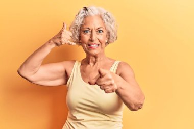 Senior grey-haired woman wearing casual clothes smiling doing talking on the telephone gesture and pointing to you. call me. 
