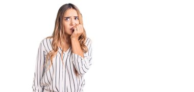 Genç, sarışın, sıradan kıyafetler giyen gergin ve gergin görünen elleri ağızdan tırnak yiyen genç bir kadın. anksiyete. 