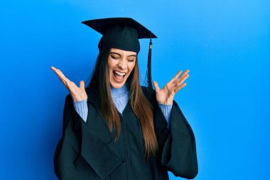 Mezuniyet şapkası ve tören cübbesi takan güzel esmer bir kadın başarı için deli ve deli gibi kutlama yapıyor. Kolları havada ve gözleri kapalı, heyecanla bağırıyor. Kazanan konsept 