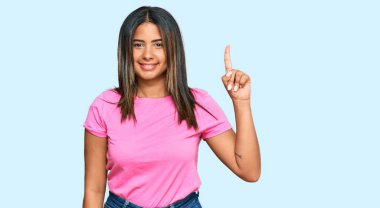 Gündelik kıyafetler giyen genç Latin kız bir numarayı gösterip işaret ederken kendine güvenen ve mutlu bir şekilde gülümsüyor.. 