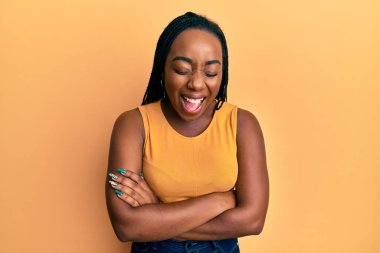Kollarını kavuşturmuş genç Afro-Amerikalı kadın gülüyor ve kahkahalarla gülüyor.. 