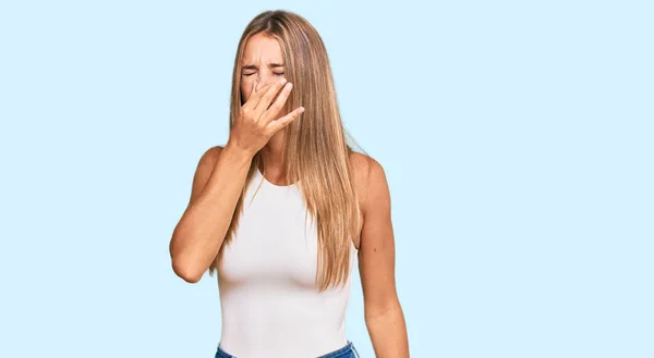 若いブロンドの女性は 眠れないシャツでカジュアルなスタイルを着て 臭いと嫌な 耐え難い匂いを嗅ぎ 鼻の上に指で息を保持します 臭いが悪い — ストック写真