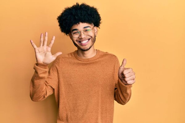 Young african american man with afro hair wearing casual winter sweater showing and pointing up with fingers number six while smiling confident and happy. 