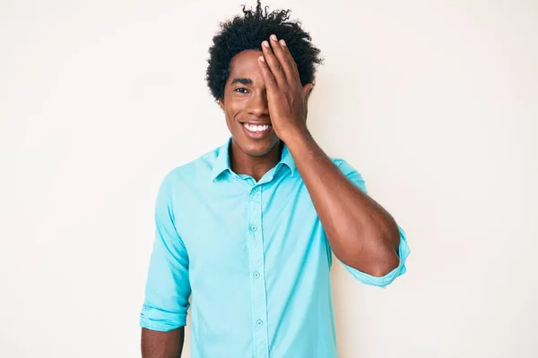 手で一つの目をカバーし 顔に自信を持って笑顔と驚きの感情を身に着けているアフロの髪を持つハンサムなアフリカ系アメリカ人男性 — ストック写真
