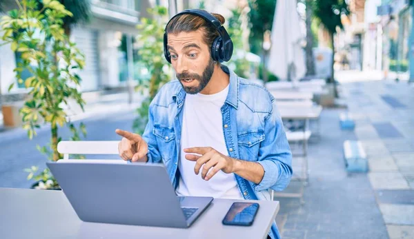 Young middle eastern man doing video call using laptop and headphones at coffee shop terrace.