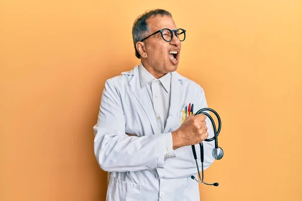医者のコートを着ている中年のインド人男性は 聴診器を怒って怒って怒り狂った叫び 怒りで叫んでいる 怒りと攻撃的な考え方 — ストック写真