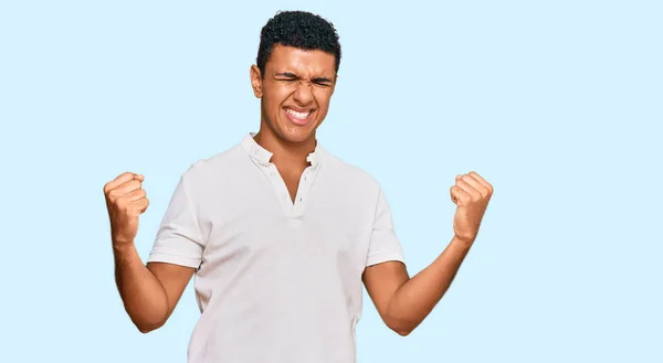 年轻的阿拉伯男子穿着休闲装 非常快乐而兴奋地做着赢家的手势 举起双臂 微笑着 尖叫着要成功 庆祝概念 — 图库照片