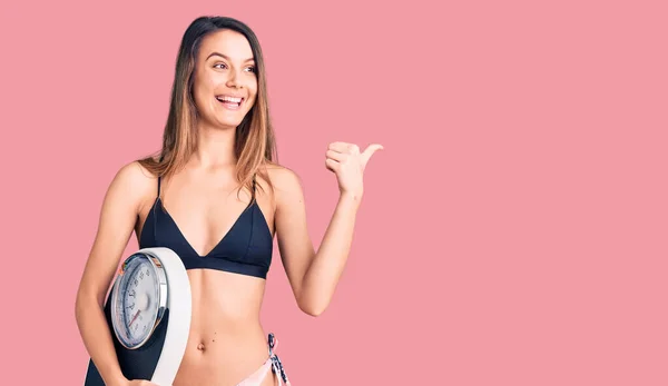 Young Beautiful Girl Wearing Bikini Holding Weighing Machine Pointing Thumb — Stock Photo, Image