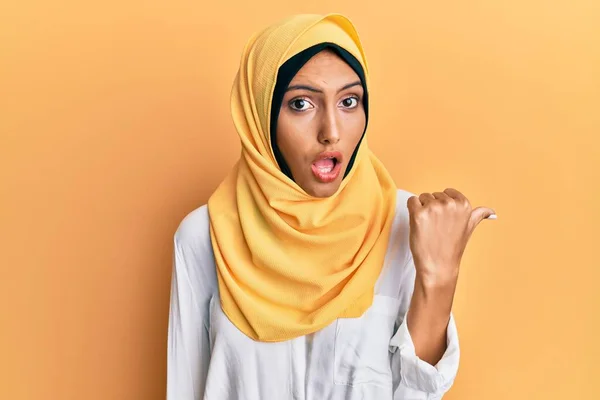 若いですブルネットアラブ女性身に着けている伝統的なイスラムヒジャーブスカーフ驚くべきポインティングとともに手指で側面に 口を開けて驚くような式 — ストック写真