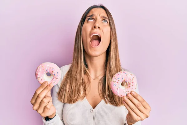 브루넷젊은 여성이 맛있는 분홍색 도넛을 소리치며 올려다 소리치고 있습니다 — 스톡 사진
