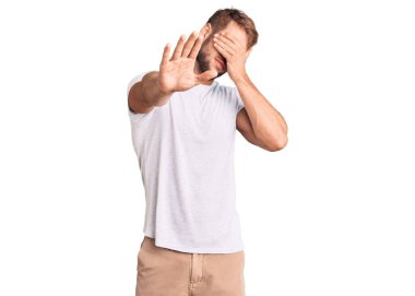 Beyaz günlük tişörtler giyen genç beyaz bir adam elleriyle gözlerini kapatıyor ve üzgün ve korku ifadeleriyle dur hareketi yapıyor. utangaç ve olumsuz kavram. 