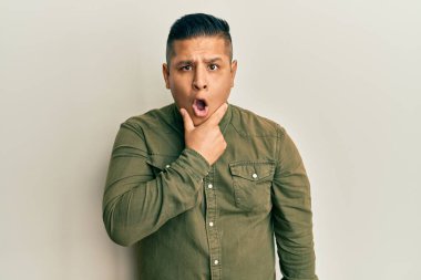 Gündelik kıyafetler giyen genç latin adam, elleri çenesinde, inanamama, şaşkınlık ve şaşkınlık dolu bir ifade takınıyor. 