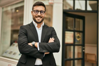 Kollarını kavuşturmuş genç İspanyol işadamı şehirde mutlu bir şekilde gülümsüyor..