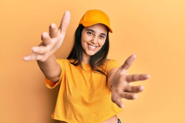 Teslimat üniforması ve şapka giyen genç İspanyol kadın kameraya bakıp sarılmak için kollarını açmış gülümsüyor. Mutluluğu kucaklayan neşeli bir ifade.. 