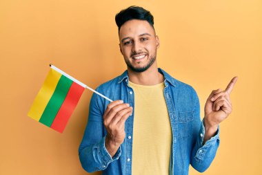 Litvanya bayrağı tutan genç Arap adam mutlu bir şekilde gülümsüyor. 