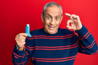 Kıdemli İspanyol asıllı adam elinde astım spreyi tutuyor. Parmaklarıyla imza atıyor, gülümsüyor ve mükemmel bir sembol oluşturuyor. 