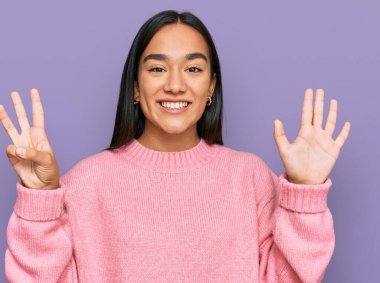 Genç Asyalı kadın, günlük kışlık süveter giyer ve sekiz numaralı parmaklarıyla gülümseyerek mutlu ve kendinden emin bir şekilde onu işaret eder.. 