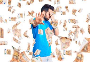 Sakallı, sıradan tişörtler giyen, elleriyle gözlerini kapatan, üzgün ve korku dolu hareketler yapan genç yakışıklı bir adam. utangaç ve olumsuz kavram.