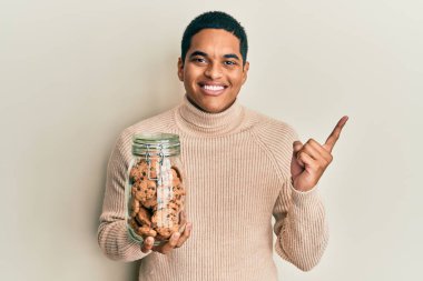 Genç, yakışıklı İspanyol adam çikolata parçacıklı kurabiye kavanozunu tutarken gülümsüyor. 