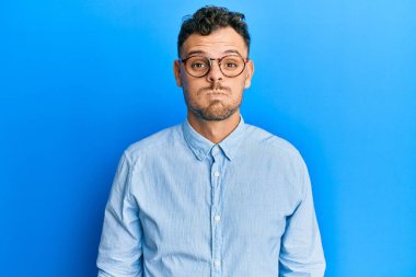 Günlük kıyafetler giyen, gözlüklü, komik yüzlü, yanak şişiren genç İspanyol bir adam. Havayla şişmiş ağız, çılgın bir ifade.. 