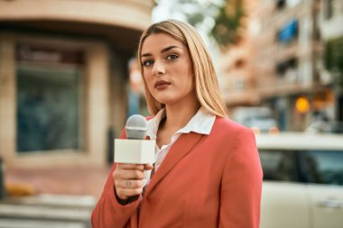 Genç sarışın muhabir şehirde mikrofon kullanarak çalışıyor..