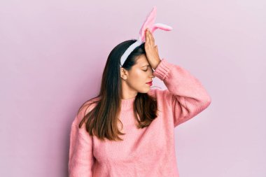 Beautiful hispanic woman wearing cute easter bunny ears surprised with hand on head for mistake, remember error. forgot, bad memory concept. 