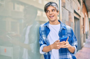 Genç İspanyol adam şehirde akıllı telefon kullanarak mutlu gülümsüyor..
