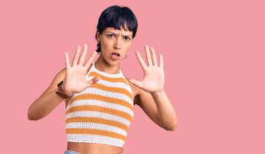 Kısa saçlı, günlük kıyafetler giyen genç esmer kadın avuç içi hareketlerini durduruyor, kızgın ve hüsran dolu bir ifade takınıyor. 