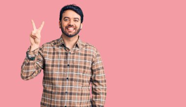 Gündelik kıyafetler giyen genç İspanyol adam iki numarayı gösterip işaret ederken kendinden emin ve mutlu bir şekilde gülümsüyor.. 