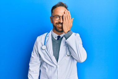 Doktor üniforması giyen yakışıklı orta yaşlı bir adam ve steteskop bir gözünü eliyle kapatıyor, yüzünde kendine güvenen bir gülümseme ve şaşırtıcı bir duygu var.. 
