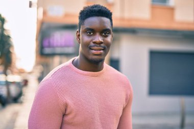 Genç Afrikalı Amerikalı adam gülümseyerek şehirde mutlu mesut duruyor..