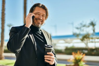 Orta yaşlı işadamı akıllı telefondan konuşuyor ve şehirde kahve içiyor..