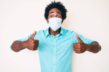 Yakışıklı Afro saçlı, tıbbi maske takmış, sevimli ve seksi bir şekilde öpüşürken kameraya bakan Afro-Amerikan bir adam. aşk ifadesi. 