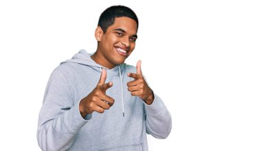 Sıradan bir kazak giyen genç, yakışıklı İspanyol adam mutlu ve komik yüzlü parmaklarını kameraya doğrultuyor. iyi enerji ve titreşimler. 