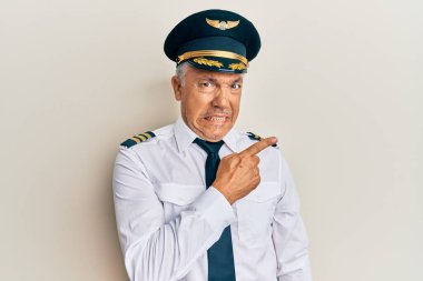 Handsome middle age mature man wearing airplane pilot uniform pointing aside worried and nervous with forefinger, concerned and surprised expression 