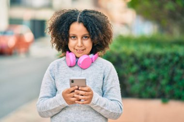 Sevimli İspanyol çocuk parkta akıllı telefon ve kulaklık kullanarak müzik dinliyor..