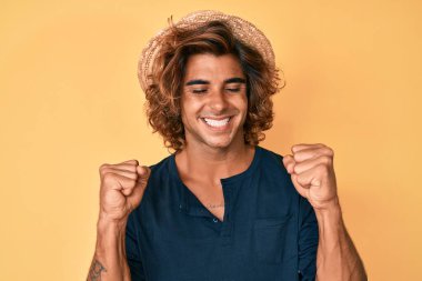 İspanyol asıllı genç adam, çok mutlu ve heyecanlı bir şekilde kollarını kaldırarak, gülümseyerek ve başarı için bağırarak kazanan hareketi yapıyor. kutlama konsepti. 