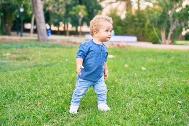 Sevimli ve mutlu küçük çocuk güneşli bir günde parkta eğleniyor. Güzel sarı saçlı erkek çocuk dışarıda oynuyor.