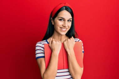 Genç İspanyol kadın elinde mutlu ve havalı bir gülümsemeyle gülümseyen bir kitap tutuyor. diş gösterme. 